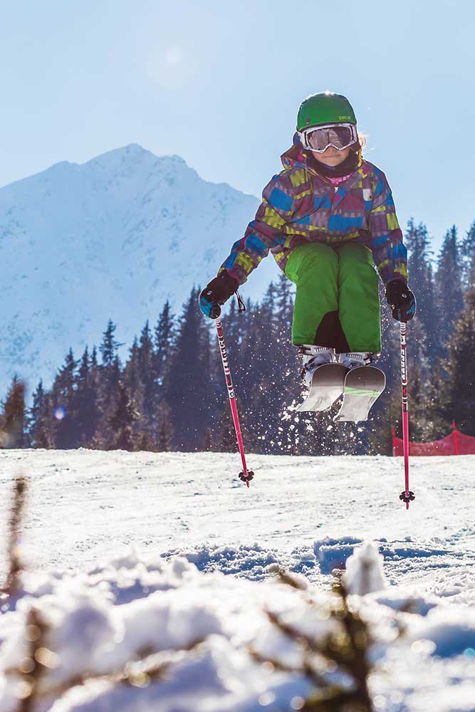 Junges Mädchen mit Skiern springt gekonnt über eine kleine Schanze