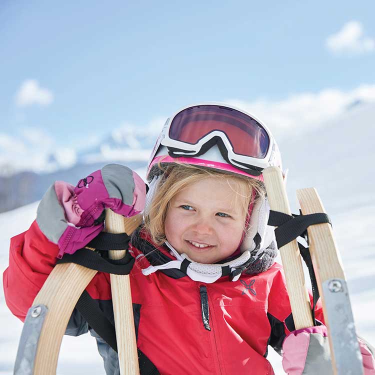 Ein kleines Mädchen mit Skihelm posiert mit ihrer Rodel für die Kamera